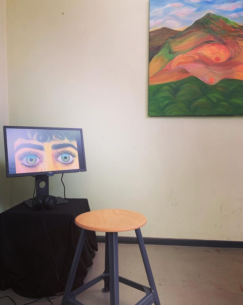 Photo of the exhibition 
left side: Monitor with the image of eyes of a woman
right side: part of a painting with landscape and a female body